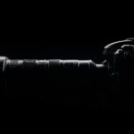 Artistic side profile of a DSLR camera with lens in dark setting.